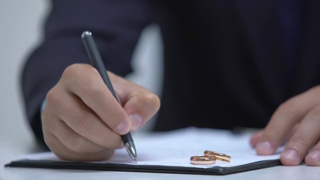 Lawyer writing marriage contract, two wedding rings lying on document, divorce