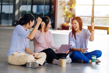 Laughing smart Asian women cozy placed on floor and rejoicing with fist up holding laptop on knees in light room