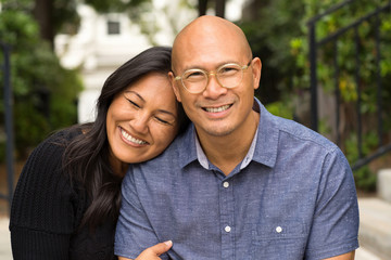 Happy Asian couple smiling and hugging outside.