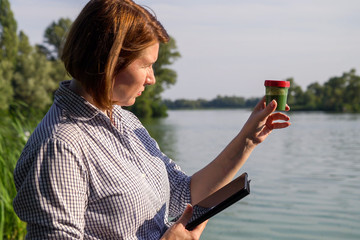 side view of researcher with tablet examines tube with green algae outside