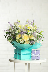 Beautiful bouquet of flowers and gift box on table against light background