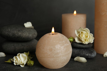 Fototapeta na wymiar Burning candles, spa stones and flowers on dark grey table