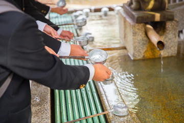 Japanese and tourist cleaning hand at holy water stone basin in front of shrine in japan shinto zen...
