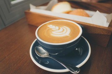 cup of coffee with latte art and tray of bread on wooden table
