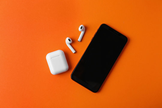 Wireless earphones, mobile phone and charging case on orange background, flat lay. Space for text