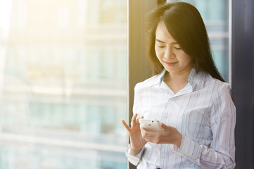 Asian busniness woman Is talking on a mobile phone by the window, there is a fair light the building window.