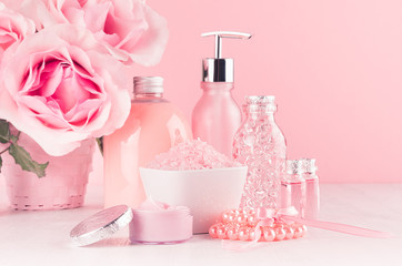 Obraz na płótnie Canvas Cosmetics products for bath, spa - essential oil, bath salt, cream, liquid soap, towel and pink roses in delicate pastel pink bathroom interior.