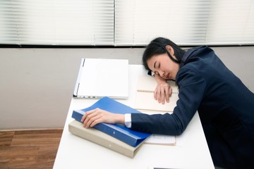 Young Asian business woman Sleep on table in office because overworking , stressed from work overload and is a tired and sleepy lady. .