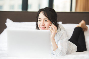 Happy asian business woman talking with cell phone laying down on the bed.