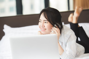 Happy asian business woman talking with cell phone laying down on the bed.