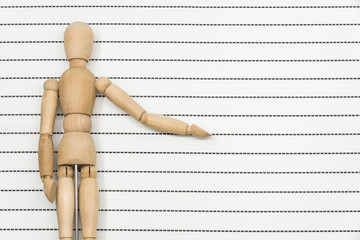 The isolated wood doll stretches out one hand and stands up on the line of white paper to form the...