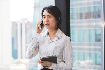 Happy asian business woman talking the phone and holding tablet computer at the working place.