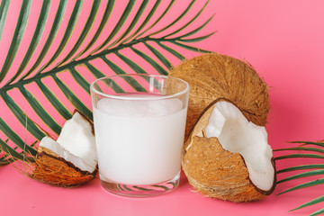 Cracked coco and coconut milk in glass on bright pink background