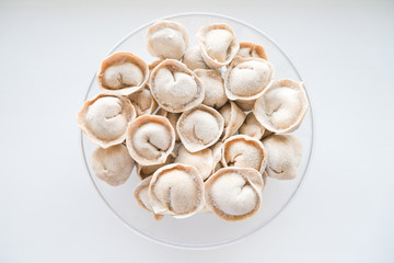 Traditional meat dumplings in a transparent plate after freezing for quick cooking. The national dish of Russian cuisine on a white background.