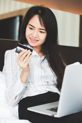 Portrait asian beautiful women are using credit cards and mobile phone to shopping online in the bedroom.