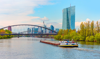 Large Cargo barge moving along the Main River with in the background beautiful view of Frankfurt am Main skyline - Frankfurt, Germany