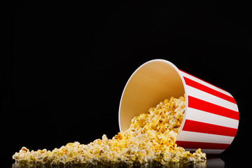 Scattered popcorn from paper striped bucket isolated on black background - obrazy, fototapety, plakaty