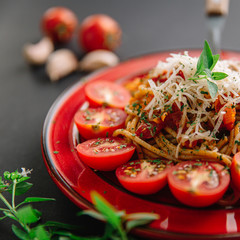 Spaghetti with cherry tomatoes, cheese and basil on dark table, close up 