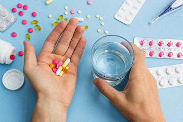 Man holding a glass of water and pills. A bunch of pills and thermometer on a blue background. Сold season, flu. Healthcare and medical concept