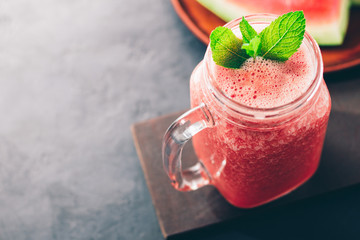 Watermelon red smoothie in jar with fresh mint leaves on dark background