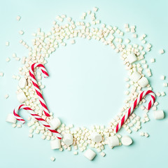 Christmas layout with candy cane and different sizes marshmallows on a turquoise background in the form of a circle shape. Concept for new year postcard with space for text.