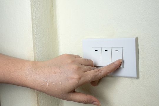 Wet hand turn on lights electric switch on white wall background