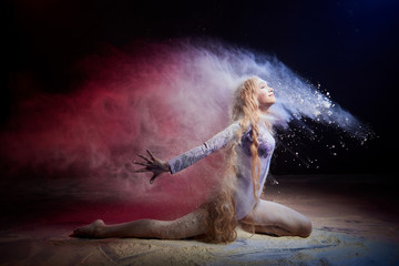 Obraz na płótnie Canvas Beautiful teen girl with long blonde curly hair in a dark room with colored lights and clouds of flour