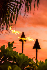 Hawaii luau party Maui fire tiki torches with flames burning against sunset sky clouds at night....
