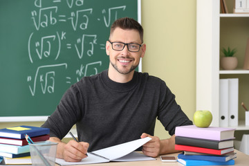 Handsome male teacher sitting at table in classroom