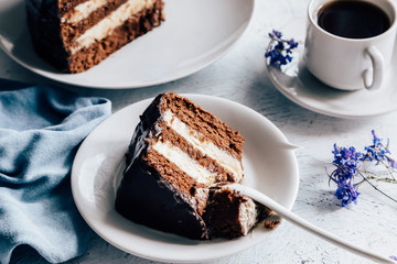 Chocolate cake on a plate and a cup of coffee and lilac flowers for decor on the table close-up