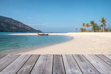Wooden tabletop on white sand beach with wooden long-tail boat in tropical sea
