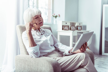 Blonde-haired elderly lady feeling thoughtful reading local news on tablet