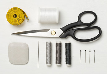 Flat lay top view sewing tools with measurement tape, chalk, thread, needles and scissors on white...