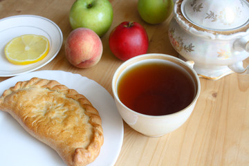 Breakfast, a cup of black tea, sugar bowl, apples, peach, pie and a slice of lemon on a wooden table, top view