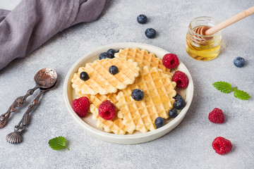 Corrugated waffle cookies with fresh raspberries and blueberries on a concrete background. Copy space.