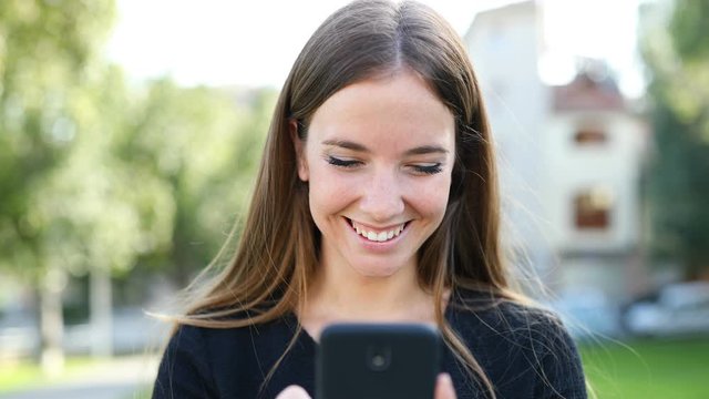 Front view of a happy woman walking using a smart phone browsing online content in the street