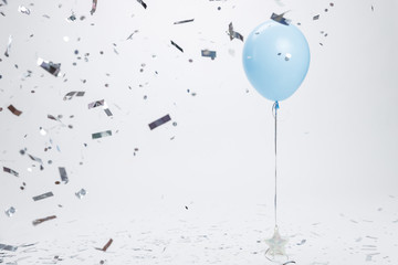 Blue balloon surrounded by silver confetti on white background. Birthday and holidays background.