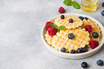 Corrugated waffle cookies with fresh raspberries and blueberries on a concrete background. Copy space.