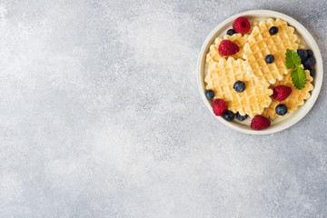 Corrugated waffle cookies with fresh raspberries and blueberries on a concrete background. Copy space.