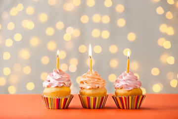 Tasty Birthday cupcakes on table against defocused lights