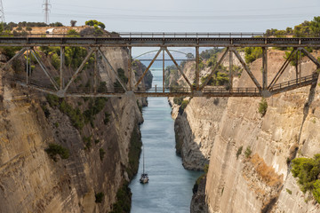 Small sailing boat passing through Corinth canal. The Corinth Canal connects the Gulf of Corinth with the Saronic Gulf in the Aegean Sea. It separates Peloponnese from the Greek mainland.