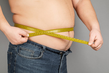 A man measures his fat belly with a measuring tape. on a gray background.