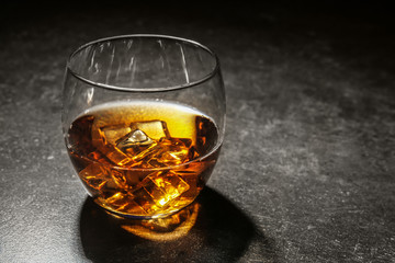 Glass of cold whiskey with ice on dark table