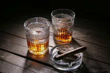 Glasses of cold whiskey with cigars on wooden table