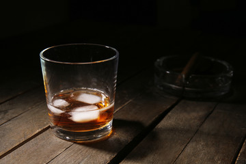 Glass of cold whiskey with ice on wooden table