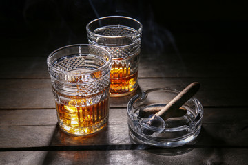 Glasses of cold whiskey with cigars on wooden table
