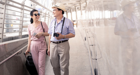 Senior Asian couple with a woman dragging a suitcase and talking happily with smiling at the airport.