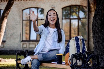Fototapeta na wymiar Hey! Hello! Teenager asian woman making greeting gesture, saying in move 'Hello' for her friends in university garden outdoor. Smiling happy face, young smart student with motivate for education.