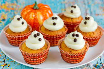 Halloween ghost cupcakes , homemade sweet pumpkin cakes with cream cheese frosting shaped funny ghosts for kid treats on Halloween party