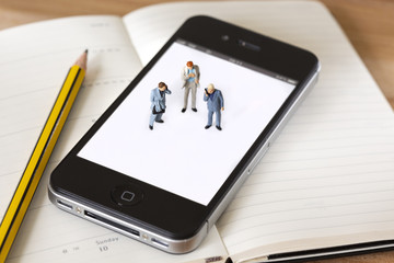 Miniature businessman standing on a cell phone with a pencil next to them having a business meeting and discussing strategys